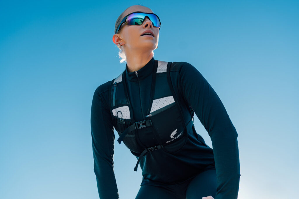 A trail runner stands confidently under a vibrant blue sky, wearing athletic gear. The scene conveys focus and readiness in the Irish countryside.