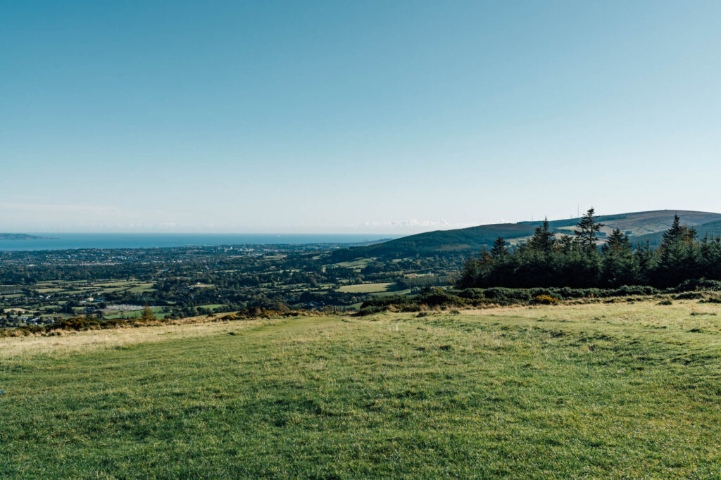 A panoramic view of rolling hills in the Irish countryside, with lush greenery stretching toward the horizon under a clear blue sky