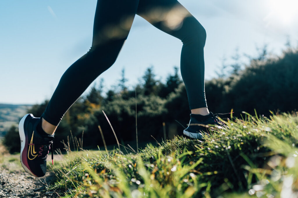 A trail anonymous runner strides confidently across a grassy field, surrounded by wildflowers and a bright sky. The image celebrates outdoor energy and freedom.