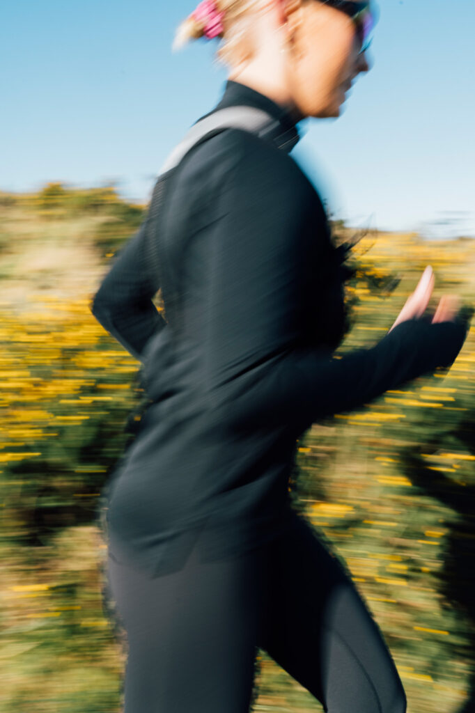 A trail runner moves through golden wildflowers on a countryside path, with motion blur emphasizing dynamic energy and speed in the rural landscape