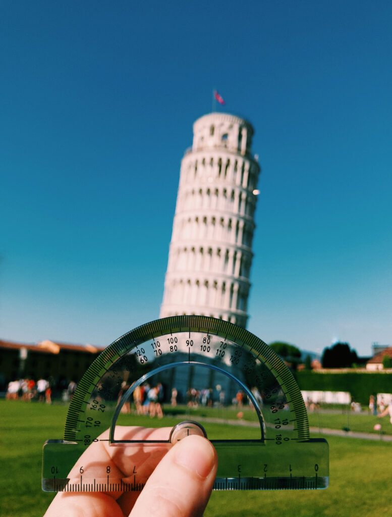 Witty picture of an hand holding a protractor to measure the angle of the leaning tower of Pisa. Picture by the artist photographer Mattia Pelizzari